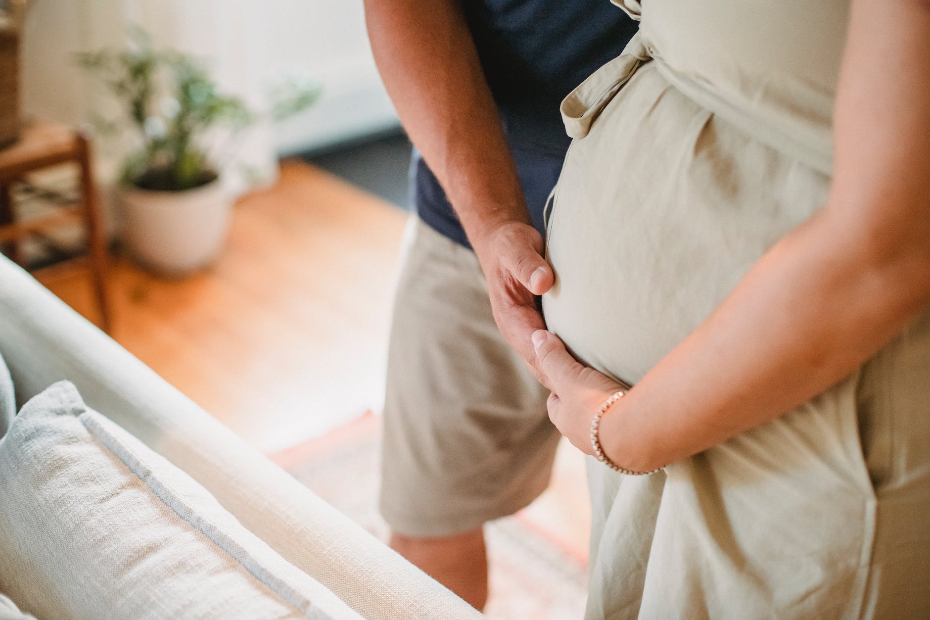 crop couple touching pregnant belly with hands at home